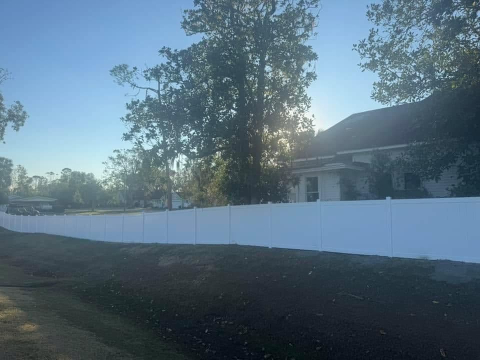 White vinyl fence lining a property under a clear sky with trees in the background.