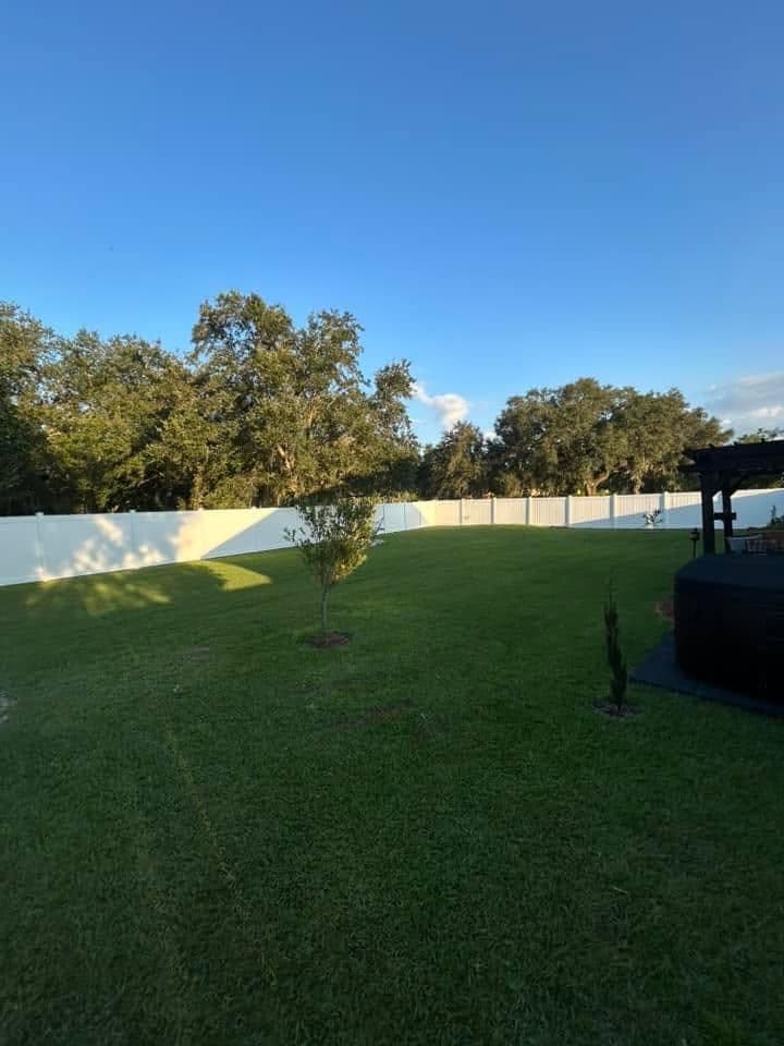 Lush green backyard with white fence, trees, and clear blue sky above.