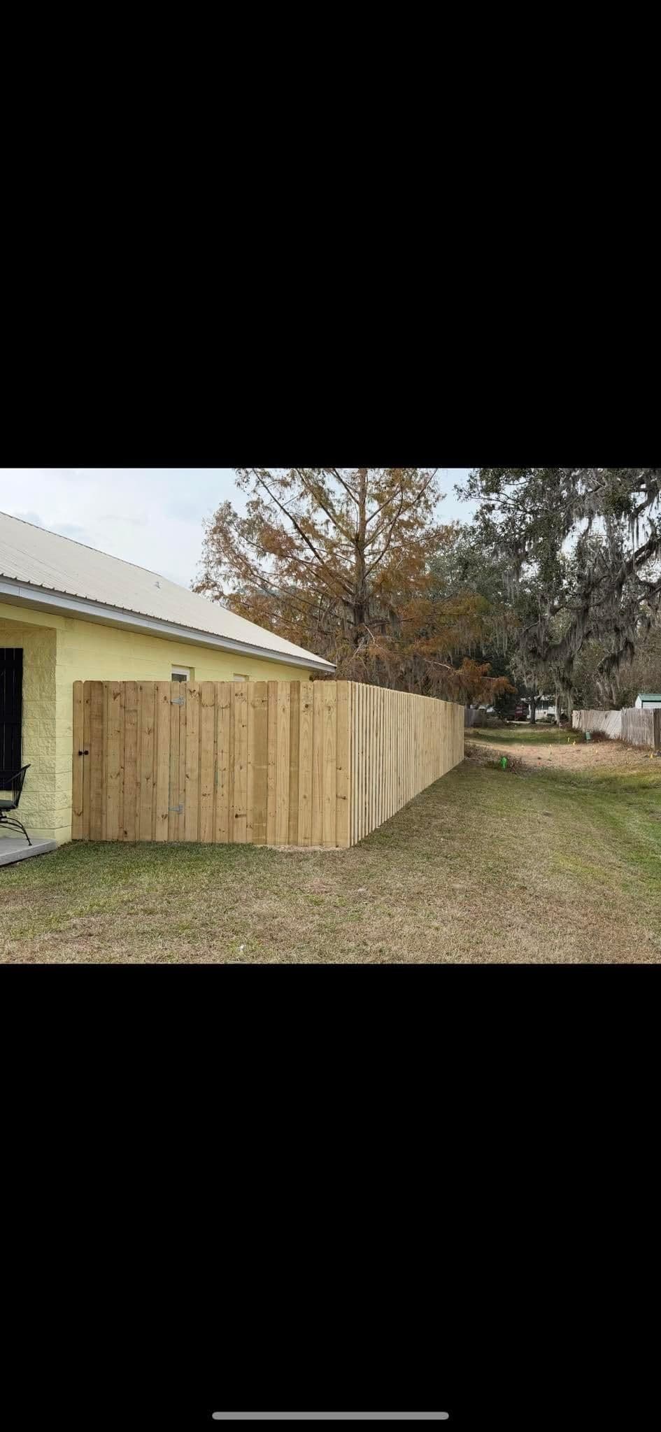 Wooden fence along a grassy yard beside a house with trees in the background.