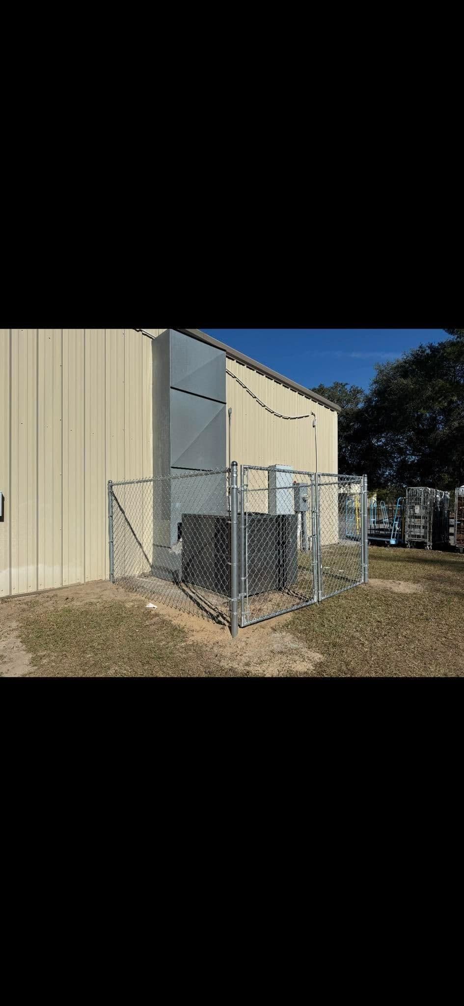 Chain link fence enclosing equipment near a metal building under clear blue sky.