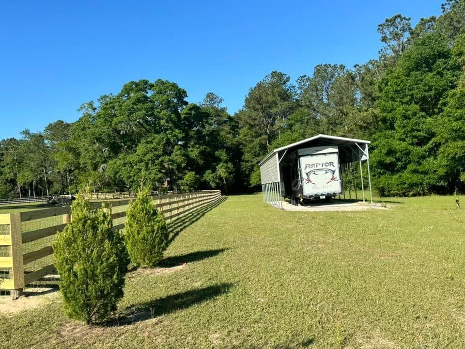 RV storage shed in a serene green landscape with trees and a wooden fence.