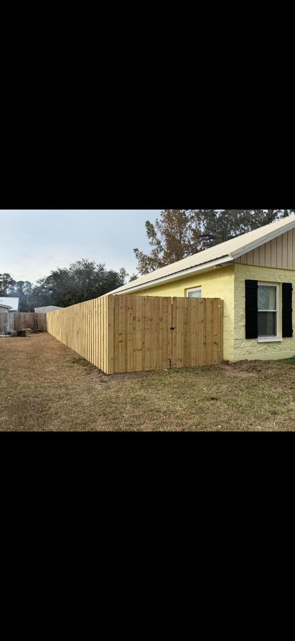 Wooden privacy fence along a residential yard with a house and grassy area.