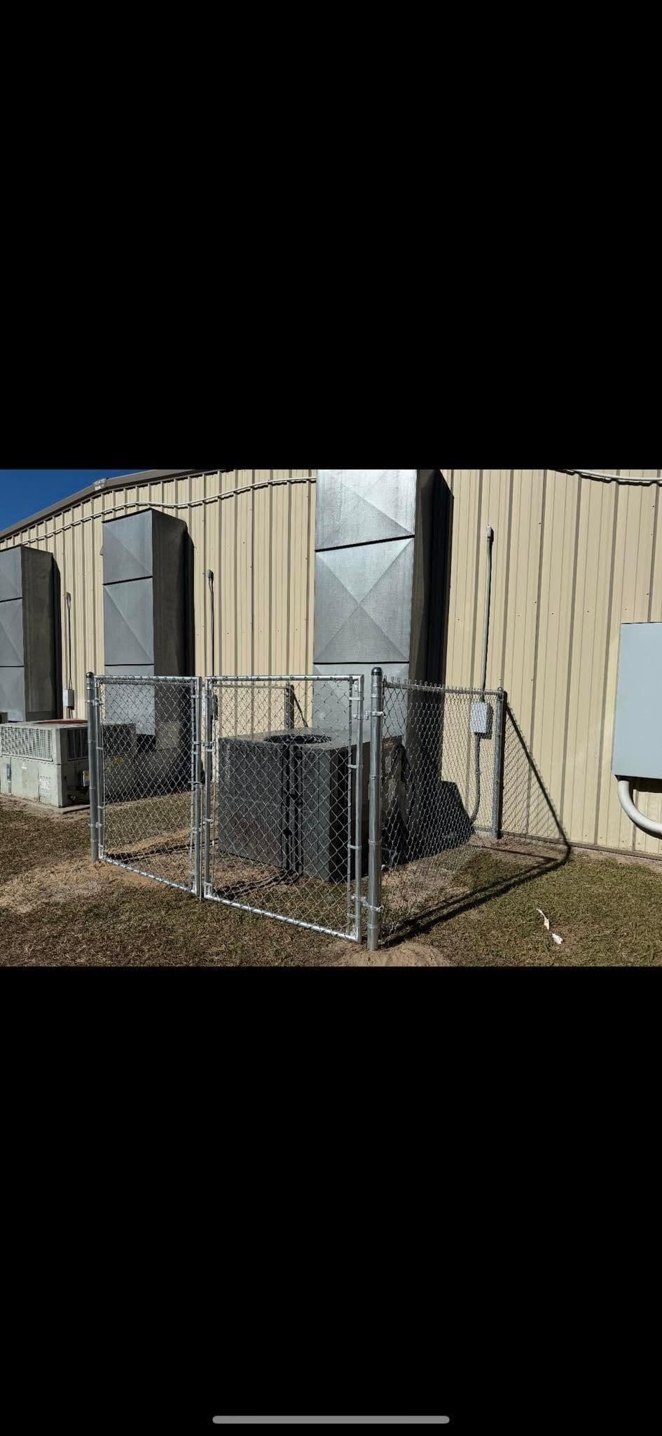 Chain link fenced area containing HVAC units beside a metal building under clear blue sky.