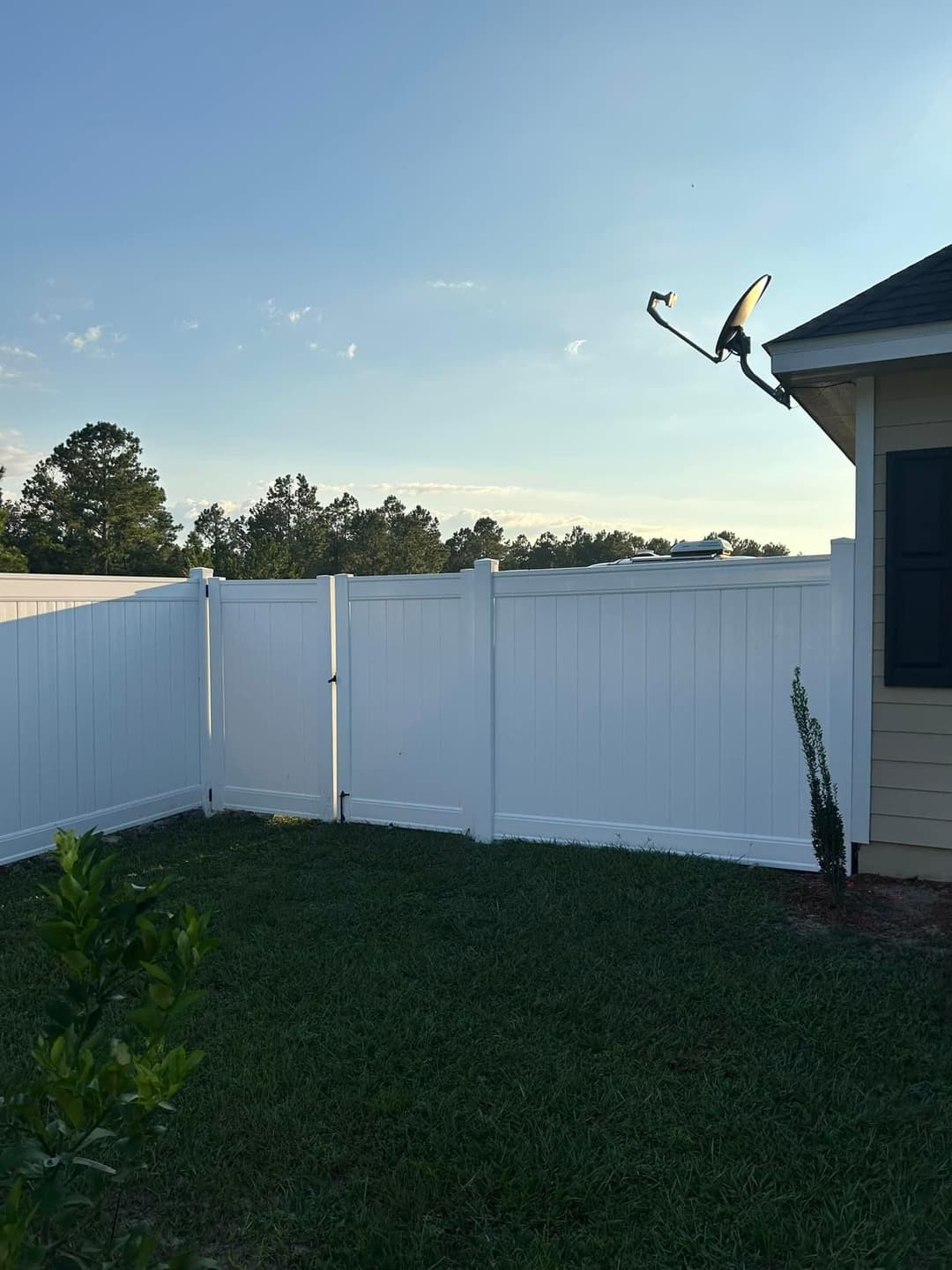White vinyl fence with satellite dish against a clear sky and green grass landscape.