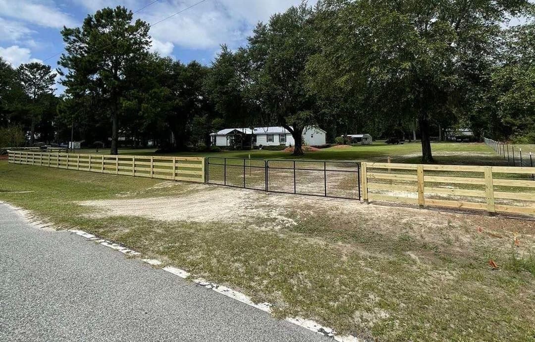 Newly built wooden fence with gate, suburban home in background, lush greenery, clear sky.