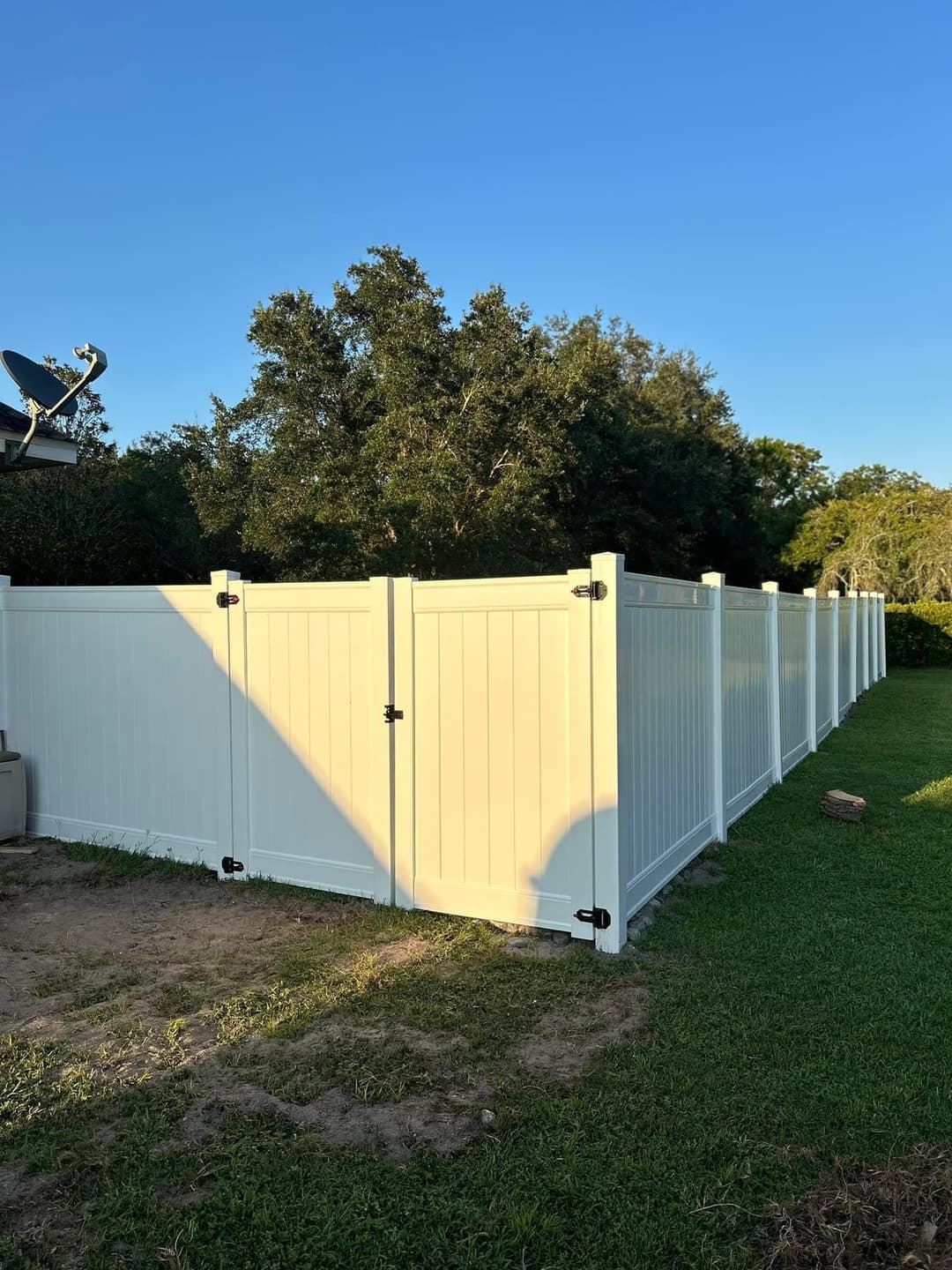 White vinyl fence surrounding a backyard, greenery and blue sky in the background.