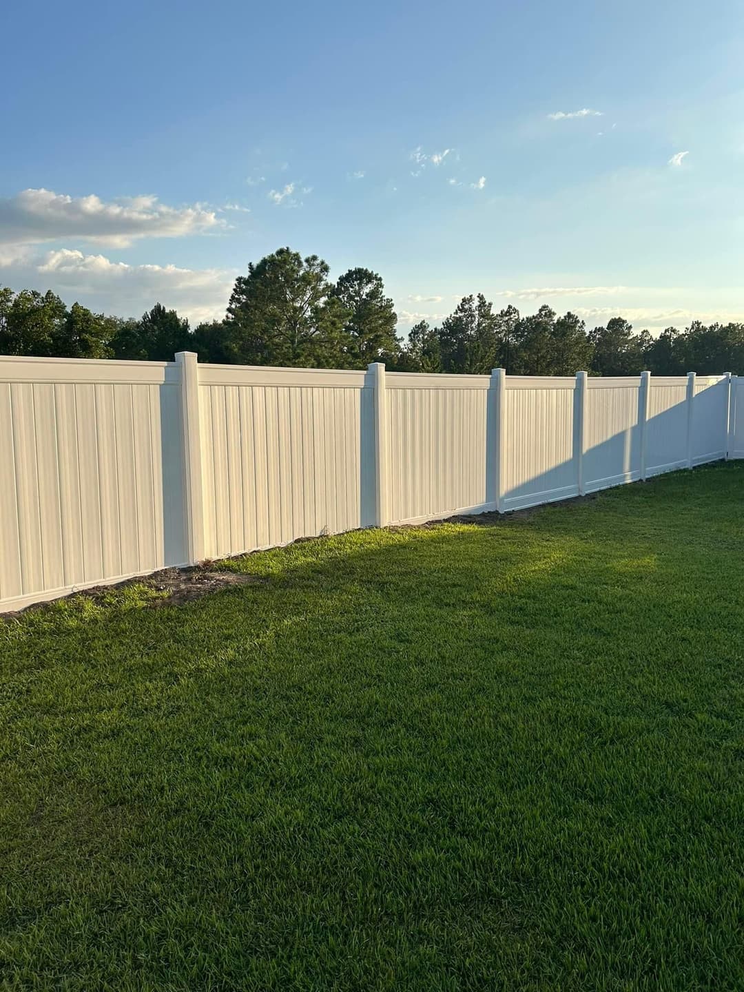 White vinyl fence extending along a green lawn under a clear blue sky.