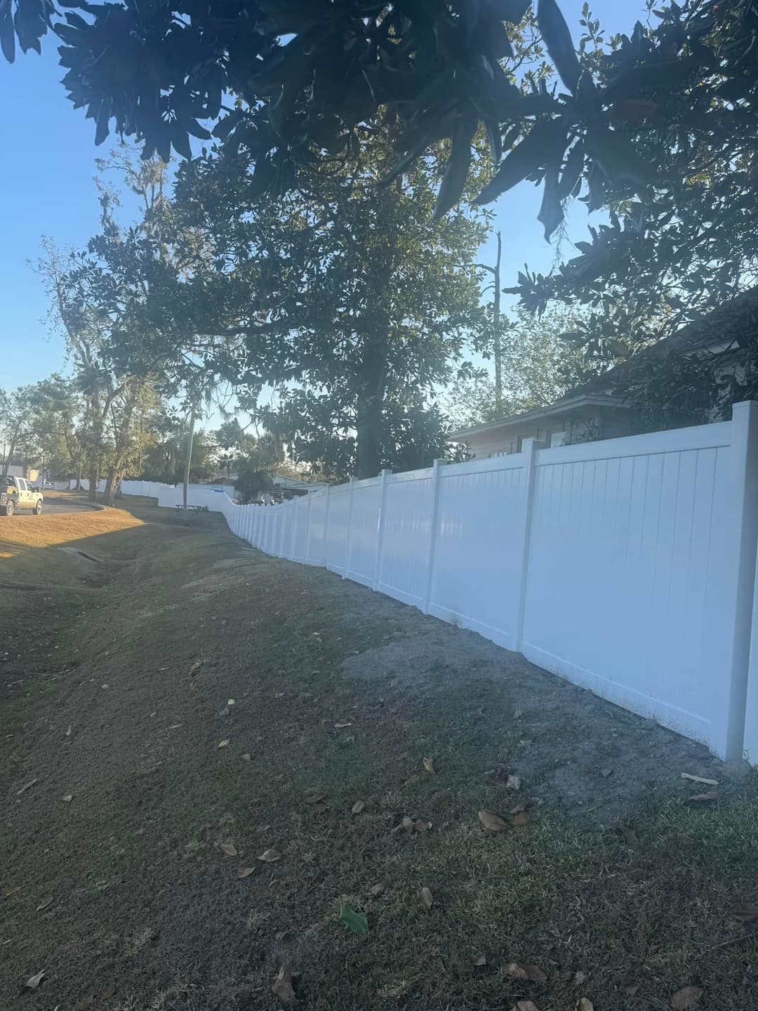 White vinyl fence along a sloped yard under a clear blue sky.
