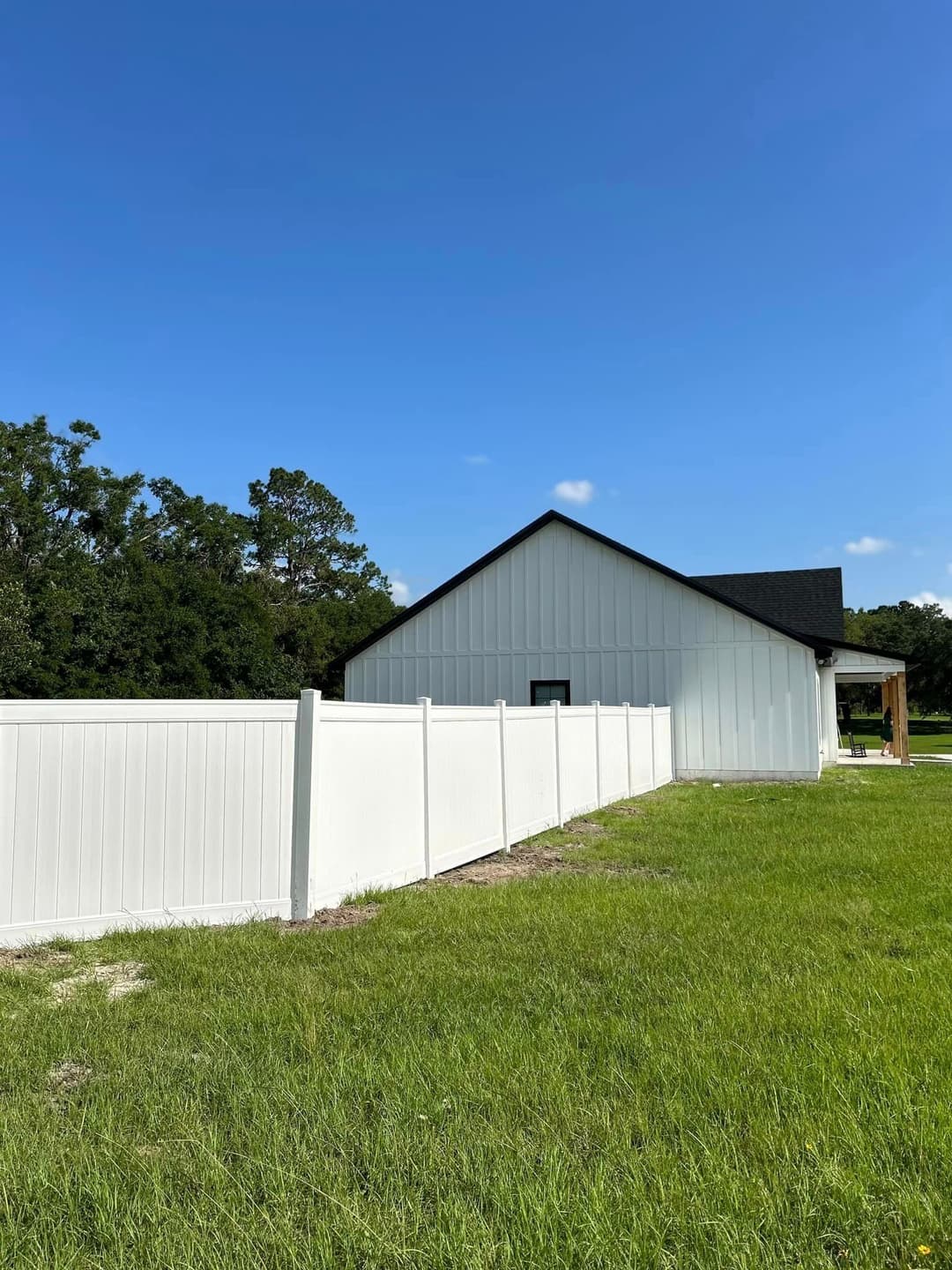 White vinyl fence surrounding a house on a sunny day with clear blue sky and green grass.