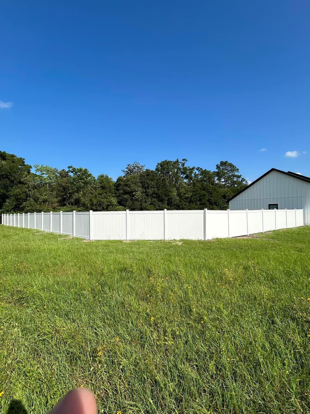 White vinyl fence surrounding a grassy area with trees and a building in the background.