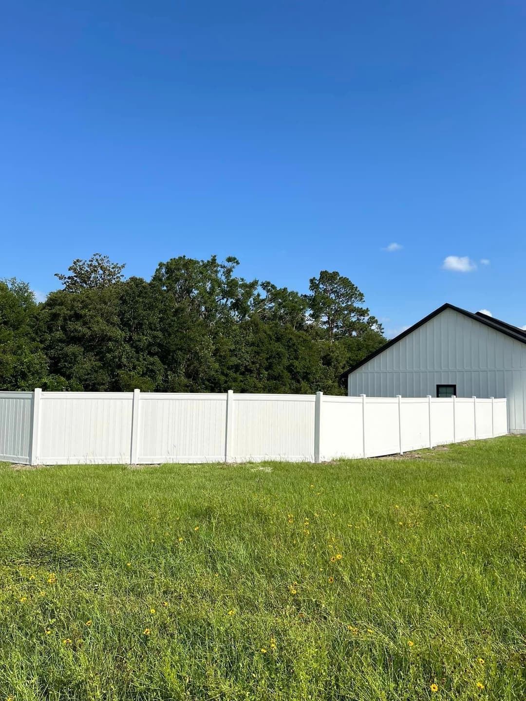 White vinyl fence surrounding a grassy area with a building and trees in the background.