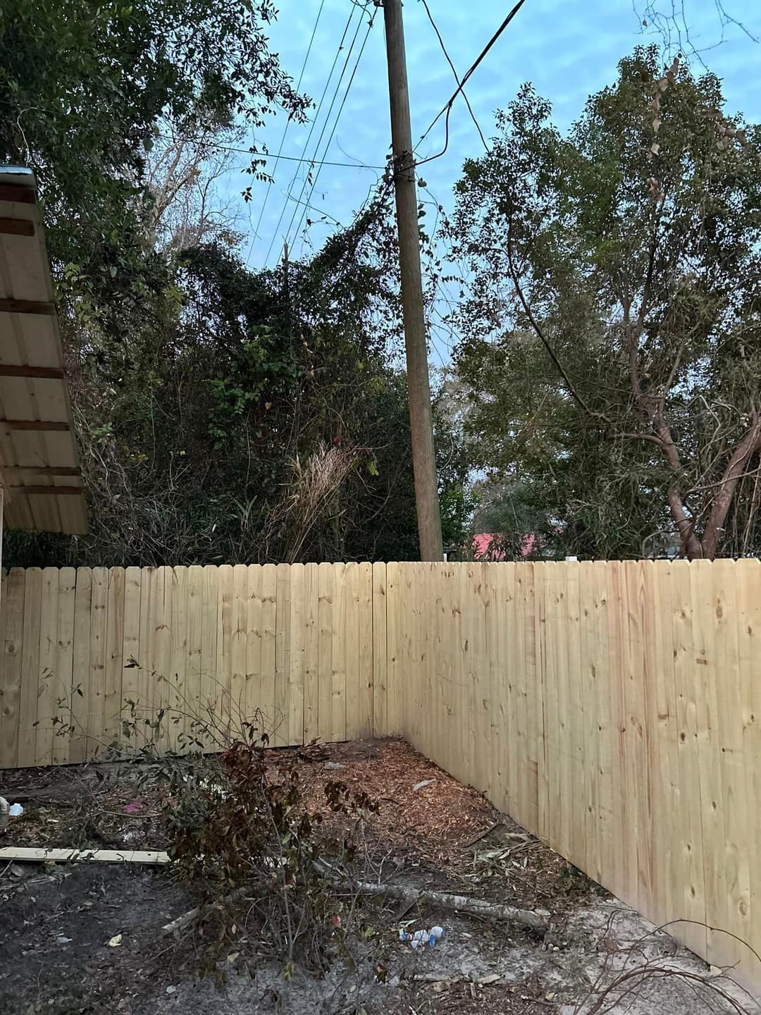 New wooden fence in a backyard with trees and power lines in the background.
