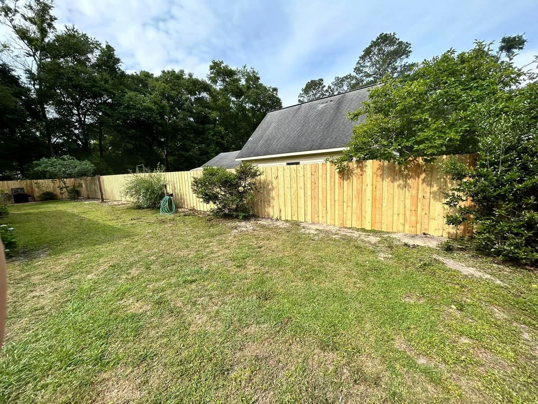 Backyard with wooden fence, lush greenery, and well-maintained lawn under a clear sky.