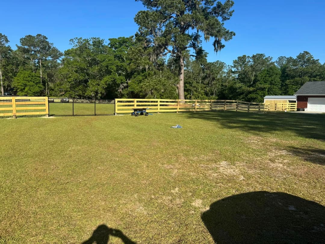 Expansive green lawn with wooden fence and trees under clear blue sky.