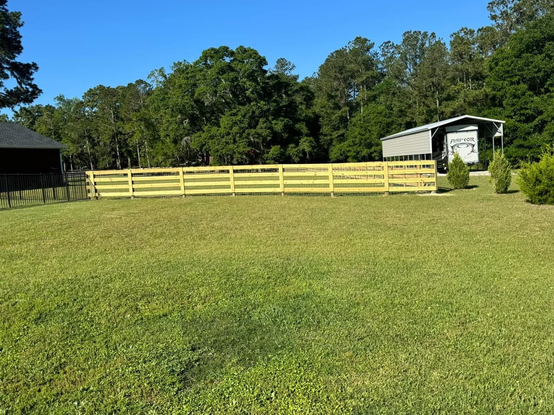 Lush green pasture with wooden fence and barn in a serene natural setting.